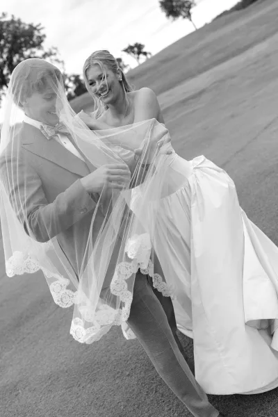 Couple portrait as an under veil wedding photo, lace veil draped over both as they laugh and lean close, capturing a playful, intimate moment.