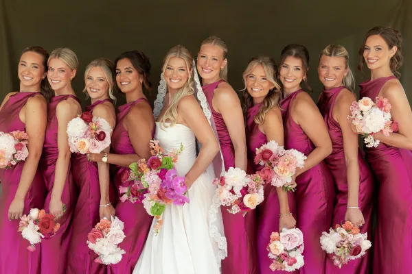 Bridal party portrait of a bride with bridesmaids in fuchsia satin dresses, arranged in a cheerful lineup.