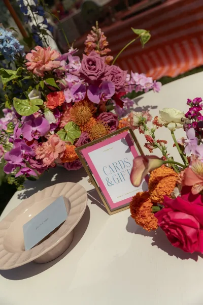 Cards and gifts sign anchors the wedding card table decor with orchids on a tabletop set on a grass lawn outdoors.