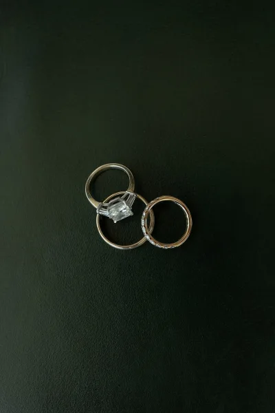 Wedding rings featuring an emerald cut engagement ring with baguette side stones arranged on a dark green surface.