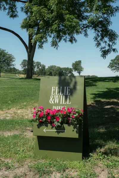 Wedding parking sign as a directional wedding sign with an arrow, on a grass lawn with trees beneath a blue sky along a dirt path.