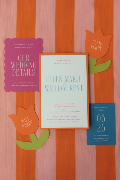 Wedding invitation suite featuring colorful wedding invitations with tulip paper cutouts, set on pink and orange striped fabric.