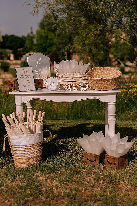 Wedding welcome table with framed wedding welcome sign, wicker baskets and paper cones on wooden crates set on a garden lawn