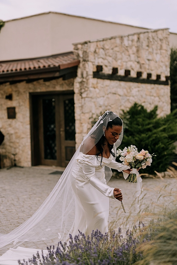 Bridal portrait of a bride in an off the shoulder wedding dress holding a bouquet in a cobblestone stone courtyard by wooden doors