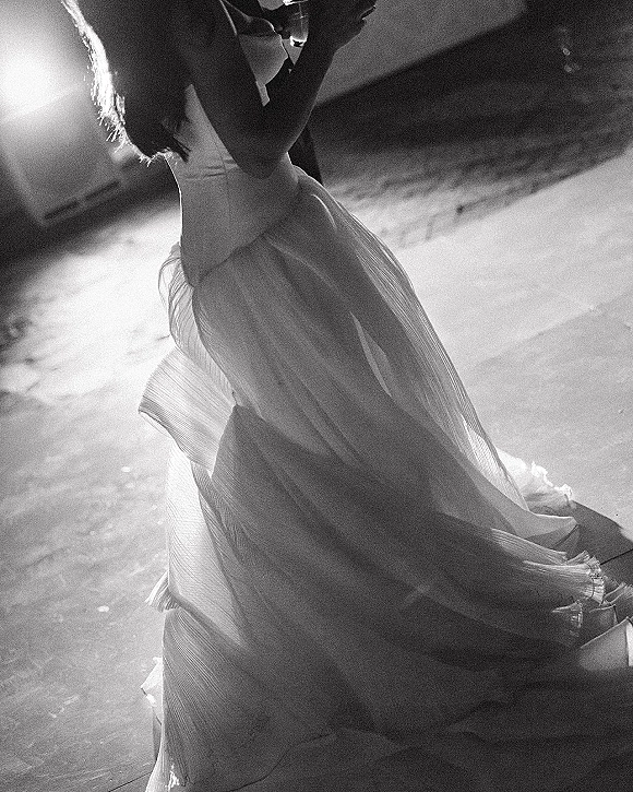 First dance as the bride and groom dancing, her wedding dress swirling beside his tuxedo under indoor reception lighting on the dance floor