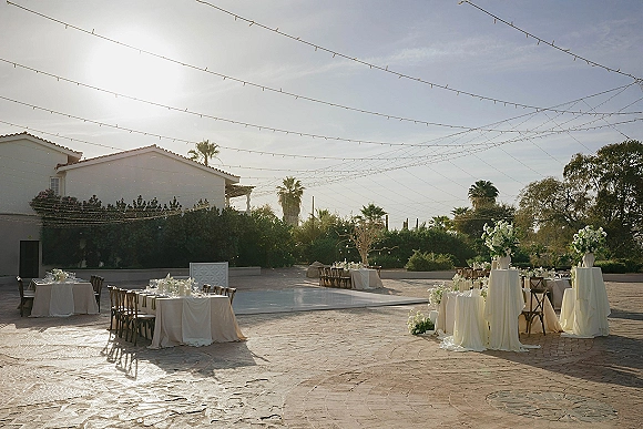 Outdoor reception decor with string light wedding reception glow over white linen tables, cross-back chairs, and a raised dance floor on a stone patio