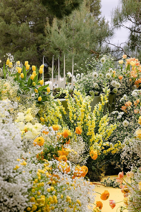 Reception tablescape with garden reception table styling, wildflower blooms, white taper candles, and glassware on green linen outdoors