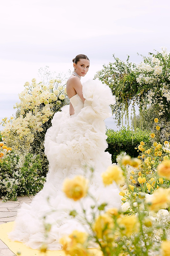 Bridal portrait of a bride in a strapless wedding dress with a voluminous tulle skirt, framed by a floral arch on a garden path