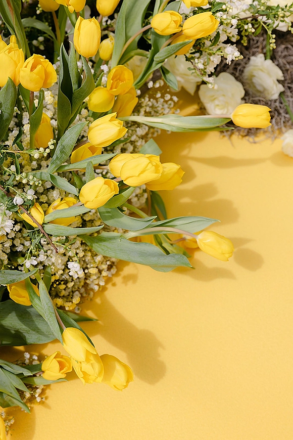 Wedding floral arrangement featuring yellow tulip wedding flowers with baby's breath, greenery, and white blooms against a bold yellow backdrop