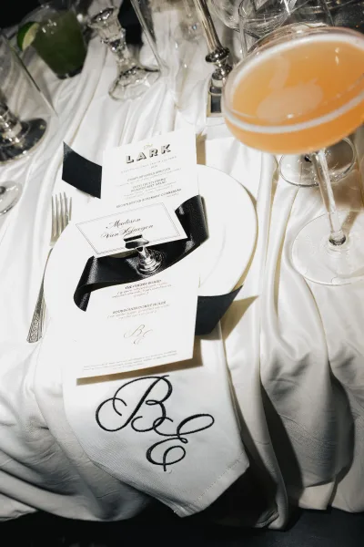 Wedding place setting with menu and place card, enhanced by an embroidered monogram napkin on a white satin tablecloth