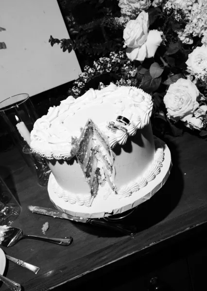 Wedding cake, a buttercream wedding cake with wedding rings beside it on a rustic wood tabletop against a brick wall.