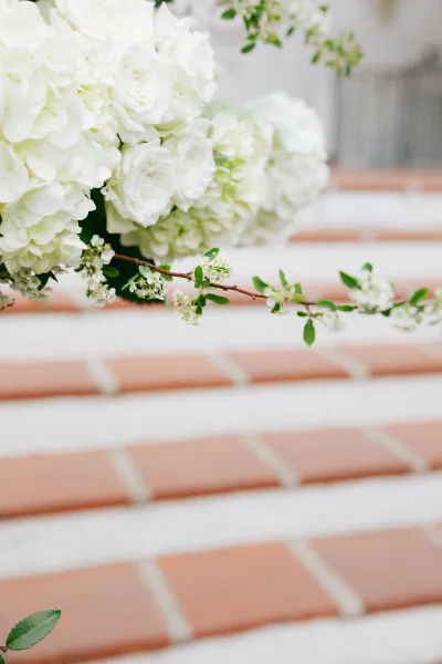Wedding flowers styled as a white floral arrangement featuring a delicate flowering branch, set on terracotta steps with white grout.