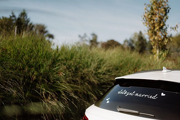 Just married car with just married car sign in handwritten window decal and heart stickers on a white rear window beside a grassy field