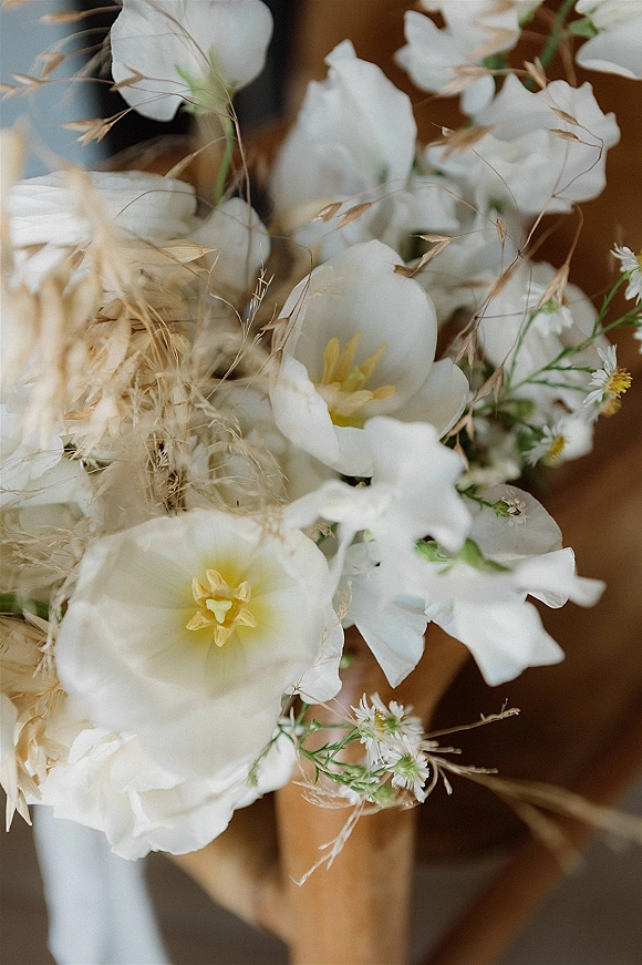 Bridal bouquet, white bridal bouquet with wildflowers and dried grasses in a hand-tied arrangement against a softly blurred indoor background
