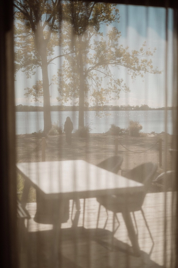 Lake wedding venue with outdoor table and chairs on a patio deck, framed by rope stanchions, overlooking trees and shoreline under open sky