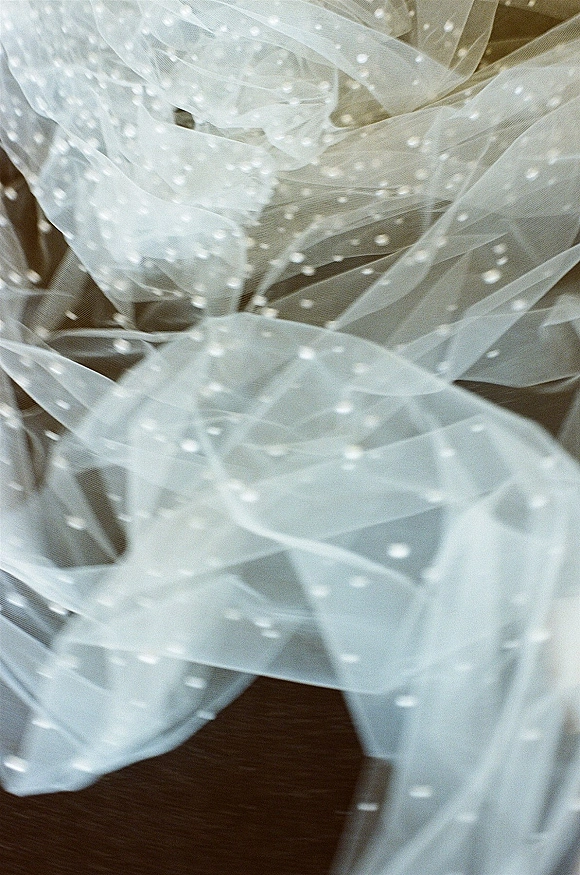 Wedding veil with dotted tulle veil and pearl dots draped on a wooden surface, sheer tulle texture shown in close-up detail