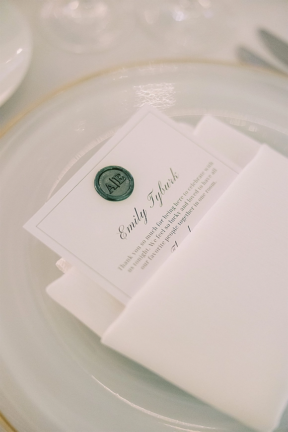 Wedding place card and calligraphy place cards tucked in an envelope with a green wax seal, styled on a white dinner plate table setting