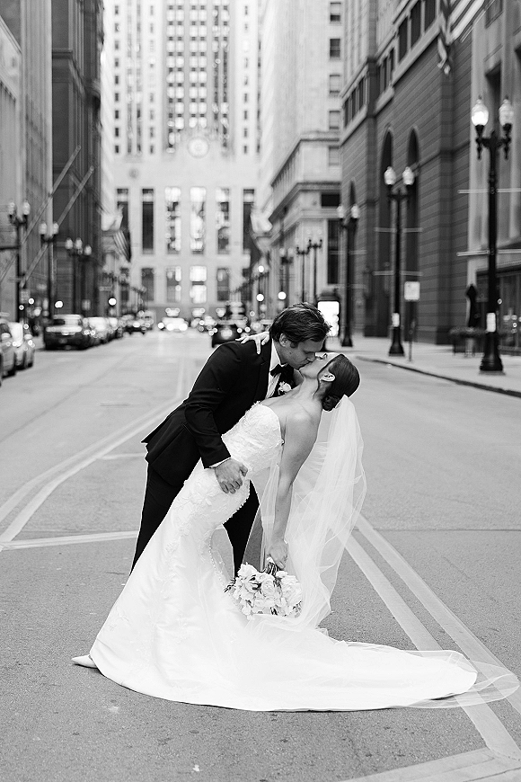 Wedding kiss portrait of a groom in tuxedo dipping the bride in a strapless dress and veil on a downtown city street with tall buildings