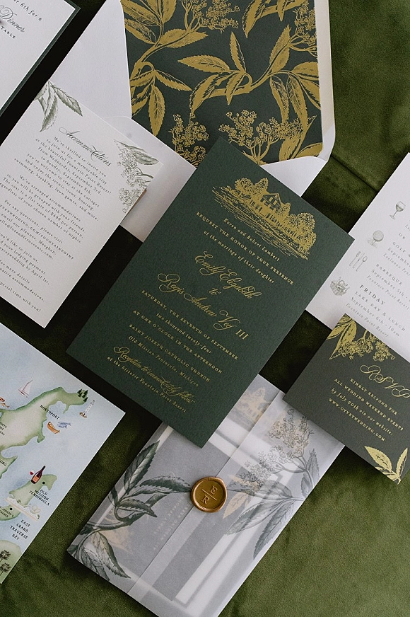 Wedding invitation suite with emerald green invitations and gold foil lettering, RSVP and map inserts, vellum wrap, wax seal on green fabric backdrop