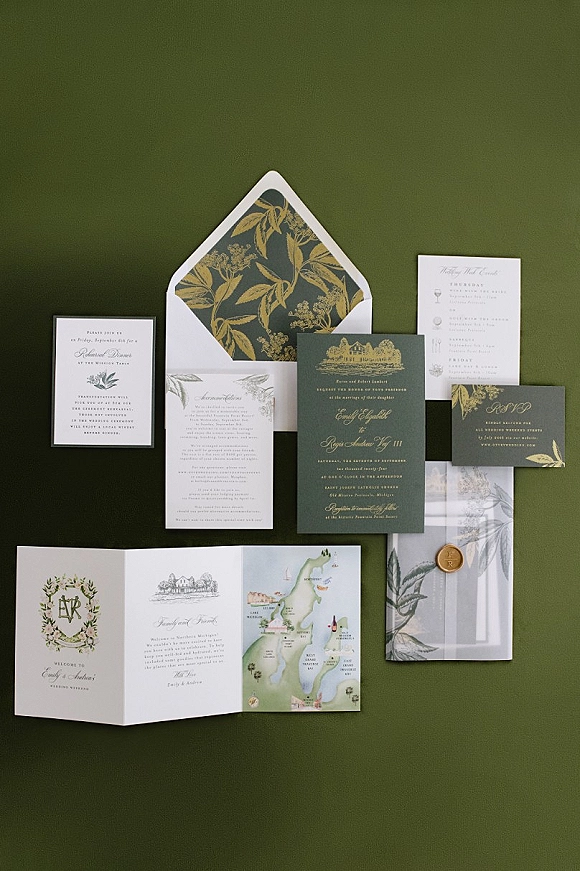 Invitation suite with green and gold wedding invitations, gold foil lettering and wax seal on envelopes with botanical liner over green backdrop