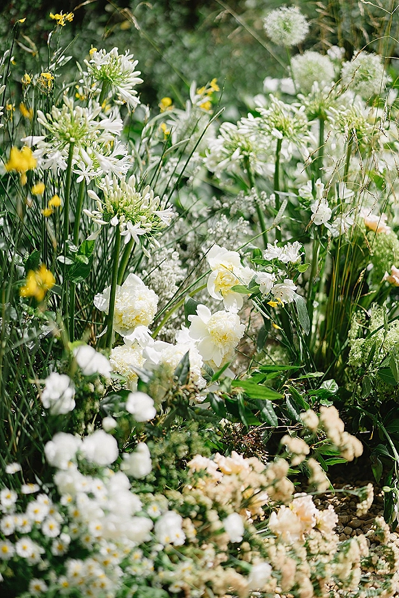 Wedding florals with wildflower wedding flowers in white blooms, greenery, and ornamental grasses arranged low on sunlit garden grass