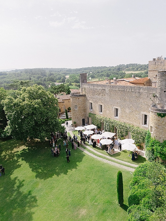 Wedding cocktail hour with outdoor cocktail hour setup under white patio umbrellas, cocktail tables on a lawn beside an ivy-covered stone building