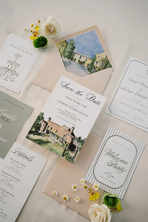 Wedding invitation suite with a save the date card, calligraphy and watercolor venue illustration, arranged with white rose on neutral fabric backdrop