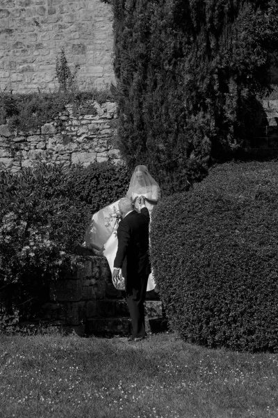 Bride descends garden steps, her blusher veil concealing her face in a black-and-white wedding photograph