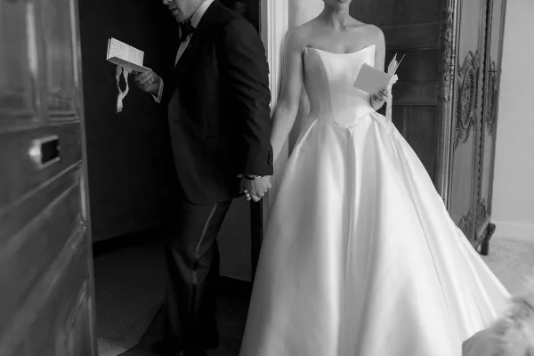 The couple share a first touch around a doorway, with ribbon-tied vow books, her strapless gown and his black tuxedo
