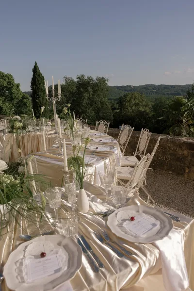 Ivory satin linens and cherries accent a reception tablescape with crystal glassware on a stone terrace