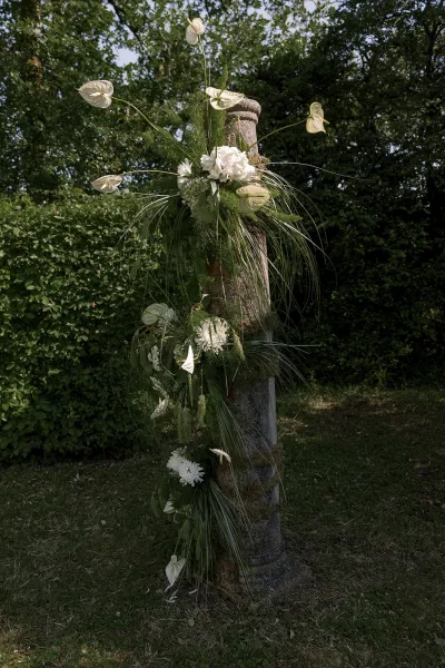 White hydrangeas and anthuriums form a floral arrangement on a moss-covered stone pillar, with trailing vines