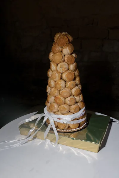 Satin ribbon wraps a croquembouche wedding cake on a gold board against a dark stone wall