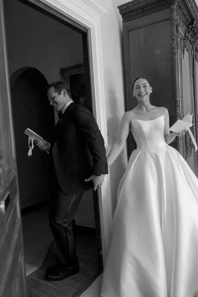 The couple hold hands through a doorway for their first touch, with ribbon-wrapped vow books in a black-and-white portrait