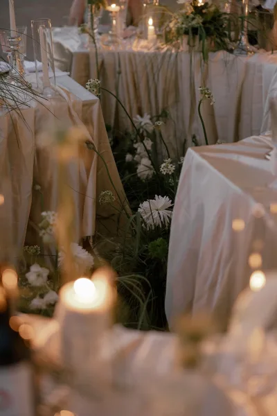 White florals and greenery decorate a reception tablescape with glass candlesticks and ivory linens under warm candlelight