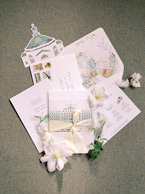 Invitation suite with letterpress wedding invitations, vellum-lined envelopes and ribbon, styled with white flowers on linen flat lay