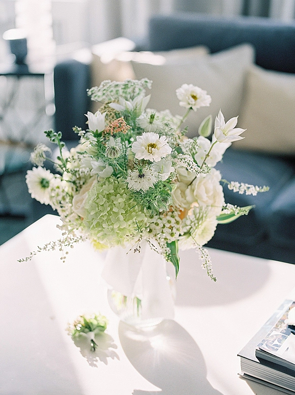 Bridal bouquet with a white and green bouquet of hydrangea and roses in a glass vase on a white coffee table in a cozy living room
