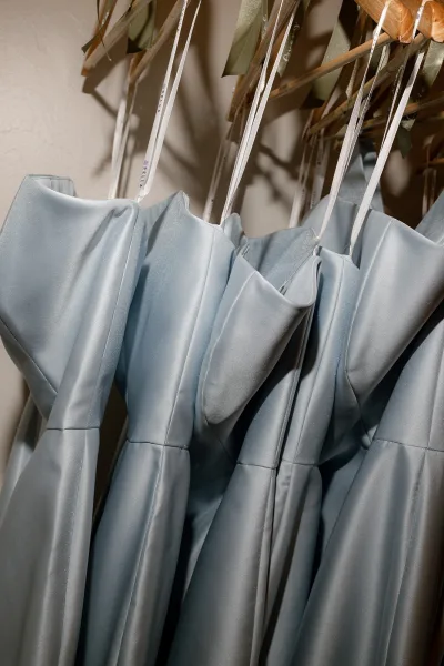 Bridesmaid dresses in a neat row, each satin bridesmaid dress finished with ribbon bows, catching soft light and subtle shadows