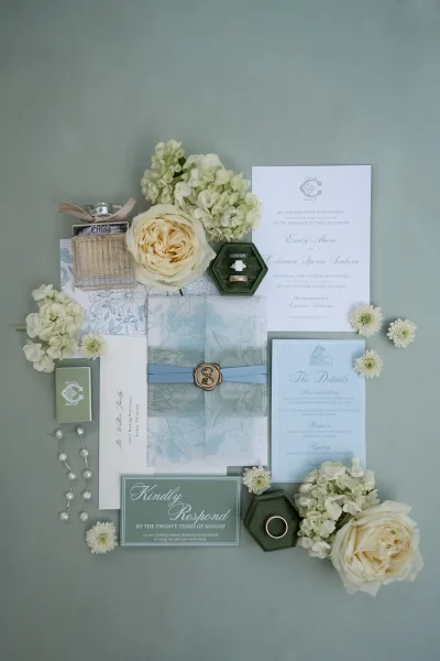 Wedding invitation suite featuring dusty blue wedding invitations, finished with a wax seal on a sage green surface.