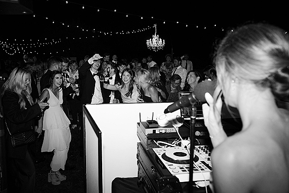Wedding dance floor at a wedding reception dancing with guests in formalwear under string lights and a chandelier in a tent at night