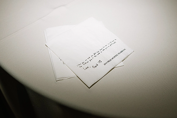 Wedding vows handwritten on folded paper card with pen ink on a white tablecloth, simple stationery detail flat lay