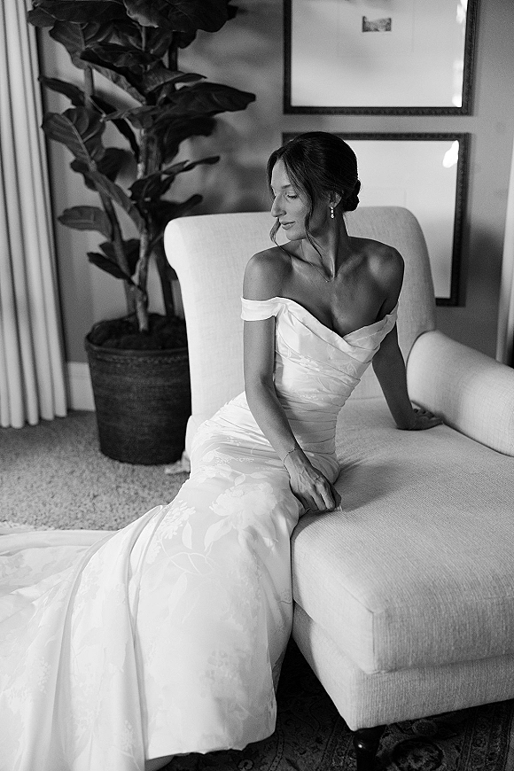 Bridal portrait in a black and white bridal portrait style, bride sitting in chair in an indoor room with curtains and framed art