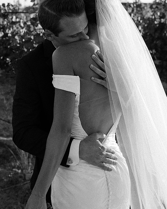 Wedding kiss portrait in a black and white wedding photo, bride in strapless dress and veil kissing groom in tuxedo amid trees