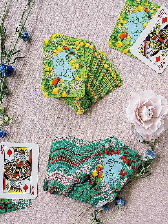Wedding playing cards arranged as a flat lay with a pink rose and floral stem accents on a linen tablecloth background