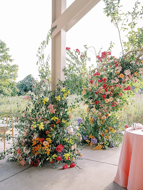 Wedding ceremony flowers on a floral ceremony arch with roses and greenery, set on an outdoor patio with wooden posts and trees
