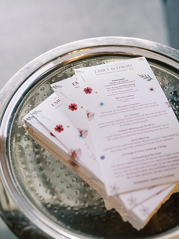 Wedding program and wedding ceremony program cards with floral and butterfly illustrations on a silver tray in soft window light