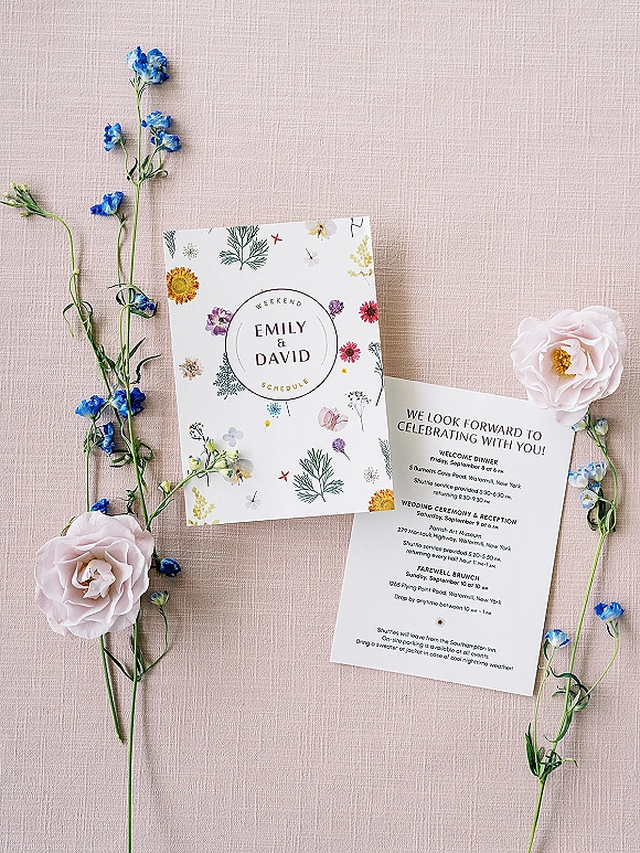 Invitation suite with floral wedding invitations and weekend schedule card, styled with blush rose and delphinium on linen backdrop