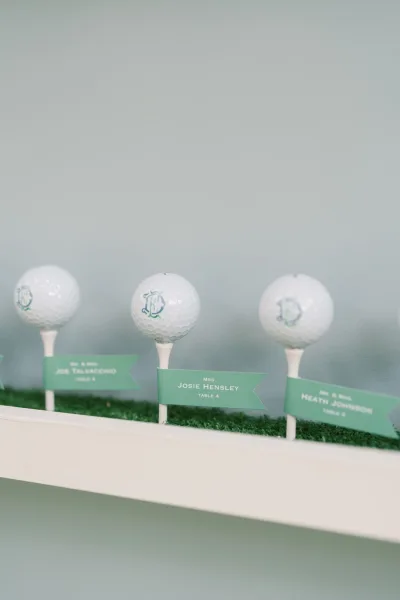Escort card display with golf themed escort cards on golf balls and tees, set on faux grass atop a white shelf against a painted wall