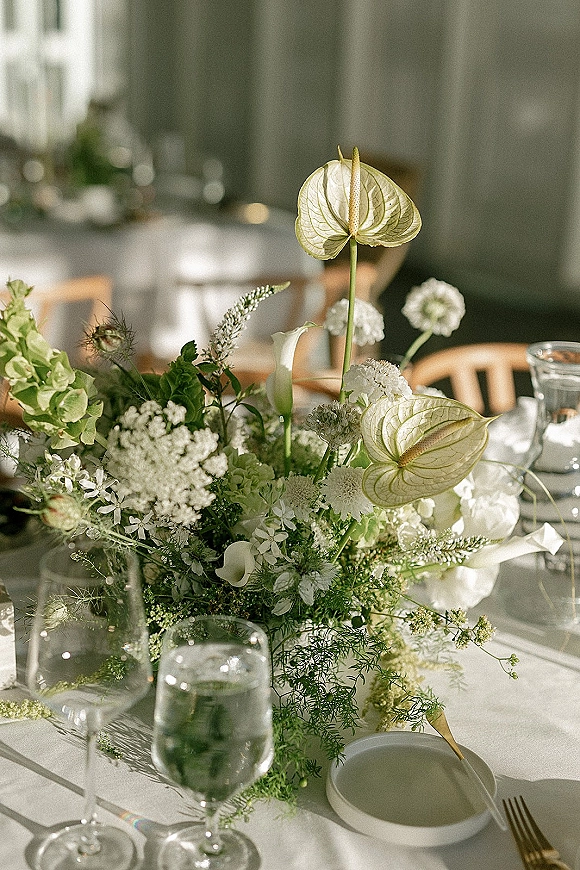 Reception centerpiece with a wedding floral centerpiece of white and green blooms, anthurium and hydrangea, set among gold flatware and glassware indoors