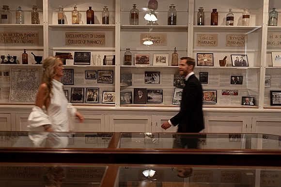First look moment as bride in a long sleeve high neck wedding dress walks toward groom in a tuxedo beside museum exhibit cases and photos