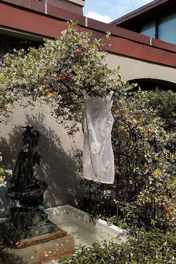 Wedding dress, beaded wedding dress hanging on a hanger with floral embroidery by a courtyard fountain and ivy-covered wall with windows